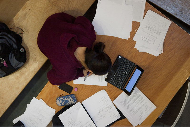 View from above: student working on homework, sitting at laptop, surrounded by papers