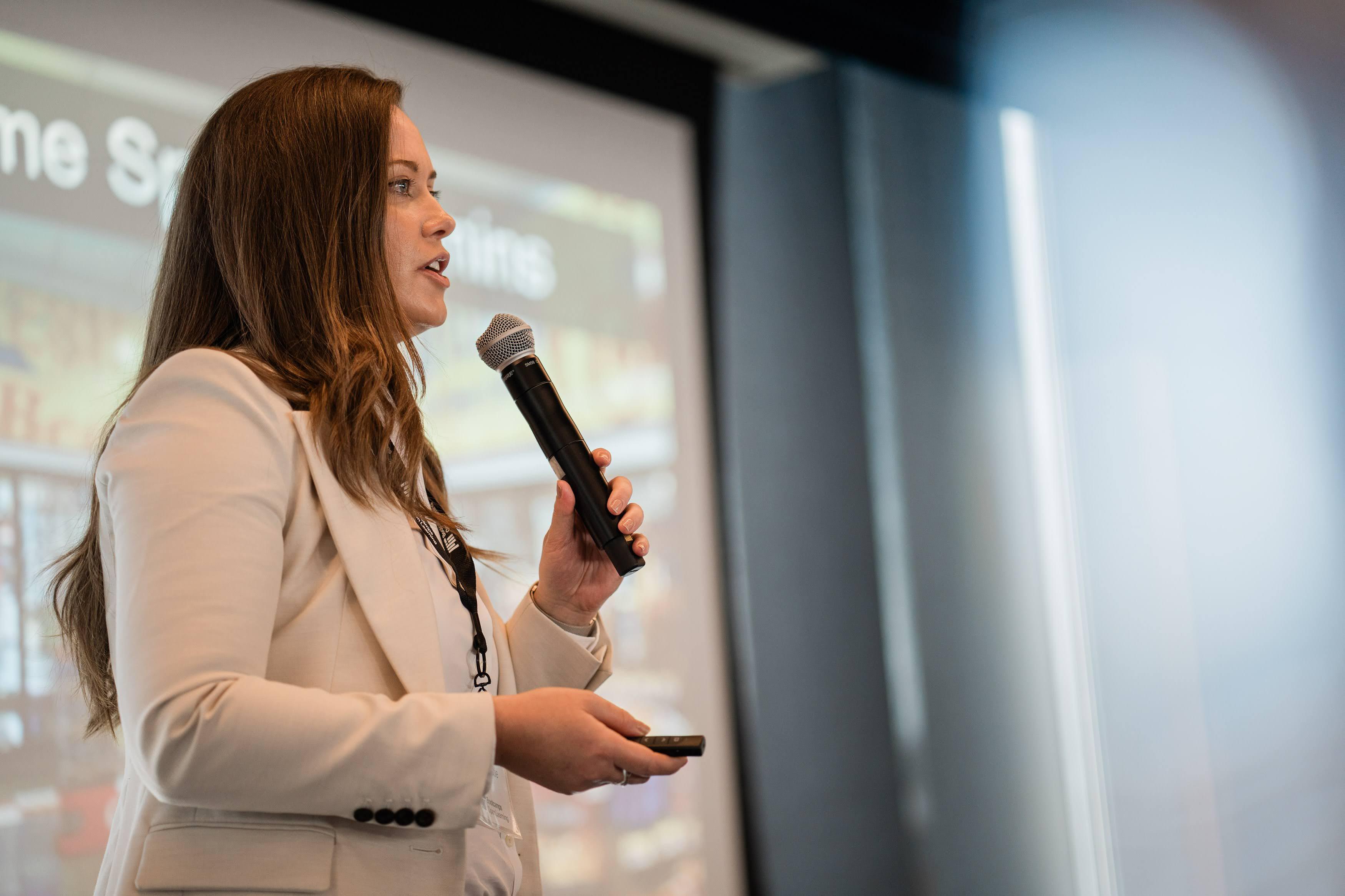 Lara Christie speaks into a microphone with a slide in the background