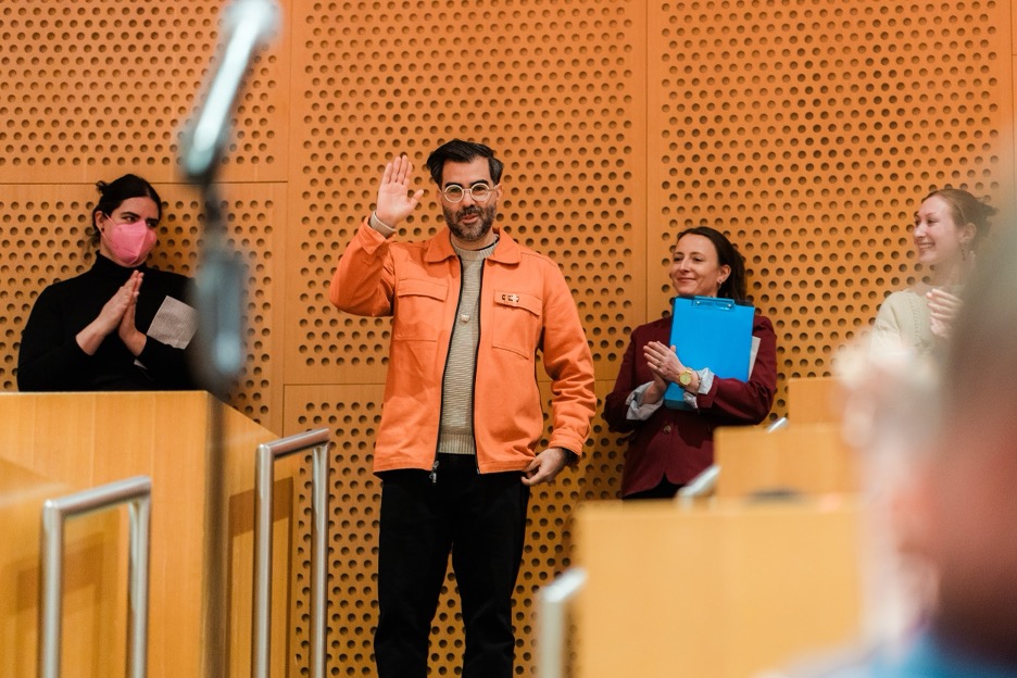 Héctor Beltrán smiling and waving as event attendees give him a round of applause.