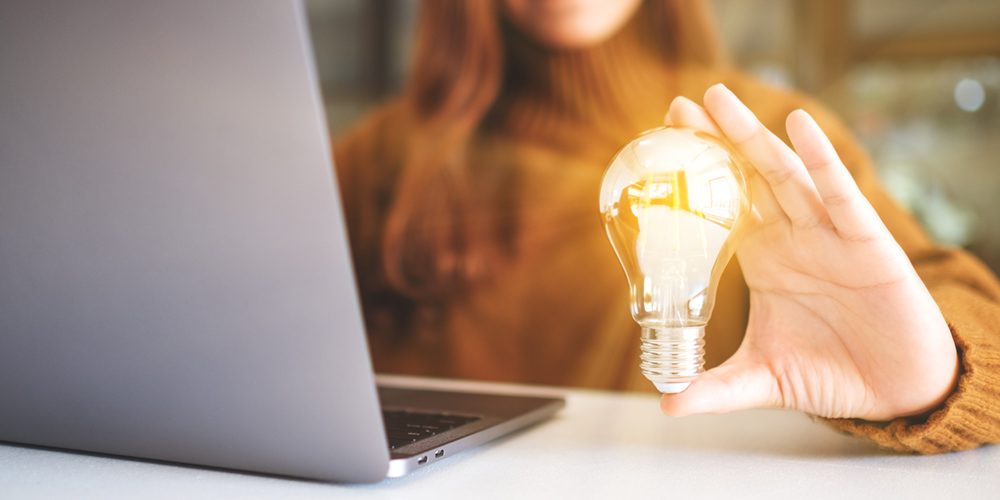 Woman holding a shining lightbulb next to a laptop