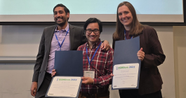 Group photo of three adults holding two paper awards in front of a projection screen that says “DEMOcon 2024, Georgia Tech, Atlanta, Georgia, USA. Exploring the integration of social practice into MOOC peer assessment. Meghan Perdue, Jessica Sandland, and John Liu (MIT, USA); Aditi Joshi (Flame University, India).”