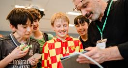 An adult shows a tablet to four young learners who are smiling 