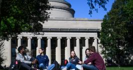 Five students sitting on the grass with the MIT Dome behind them