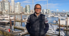 Badri Ratnam stands in front of a marina with buildings and water in the background.