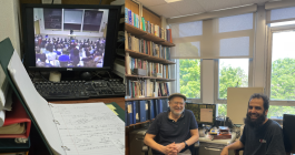 A side-by-side collage of two scenes in an academic setting. On the left, a desk holds an open binder filled with handwritten notes, positioned in front of a computer monitor displaying a crowded lecture hall with a professor at the front. On the right, two men sit and smile in a book-lined office with large windows.