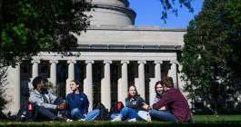 A group of 4 students sit on the lawn in front of the MIT dome