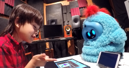 Boy sits playing on a tablet, along with a furry robot companion