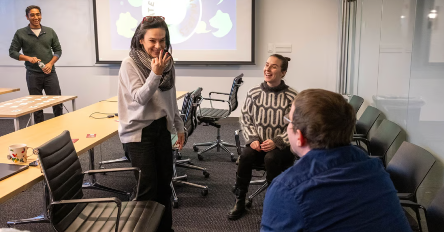 Candid photo of four teachers in a classroom setting playing charades. A screen in the background says "climate change charades."