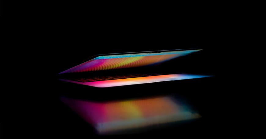 Glowing, multi-colored half-closed laptop sitting on a black, reflective surface.