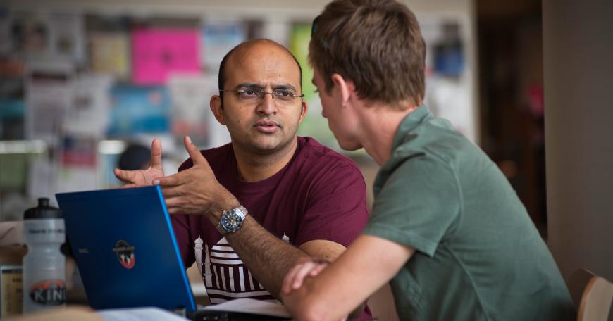 Two learners sit at a laptop, discussing finance.