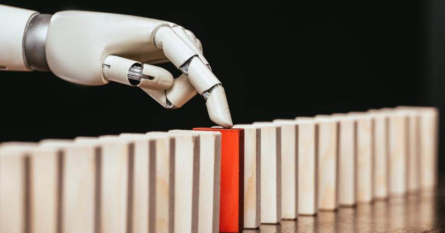 Photo of a robot hand singling out one domino in a row of dominoes standing up.