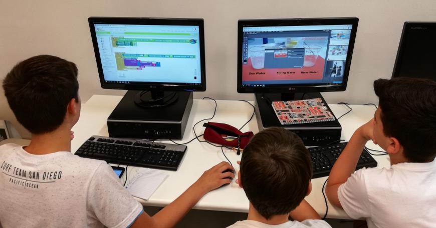 Three middle school-aged male students seated at two computers, rear view