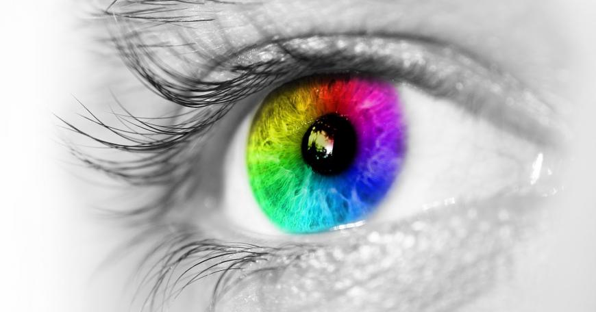 Black and white close up of an eye, with the iris in rainbow colors