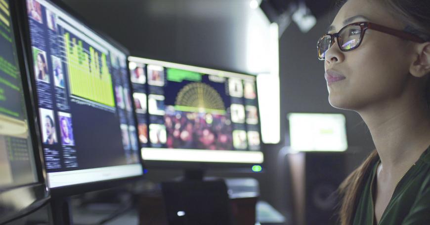 Woman surveys data across several computer screens