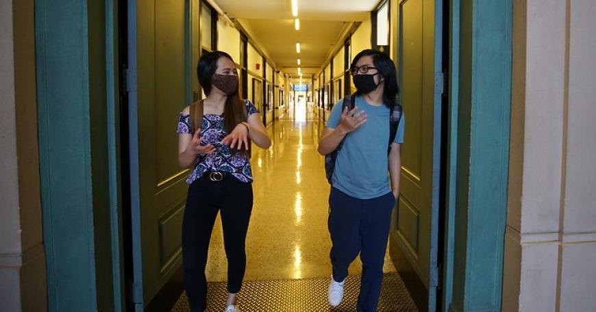 Two students in face masks stand at a distance from each other while exiting the Infinite Corridor.