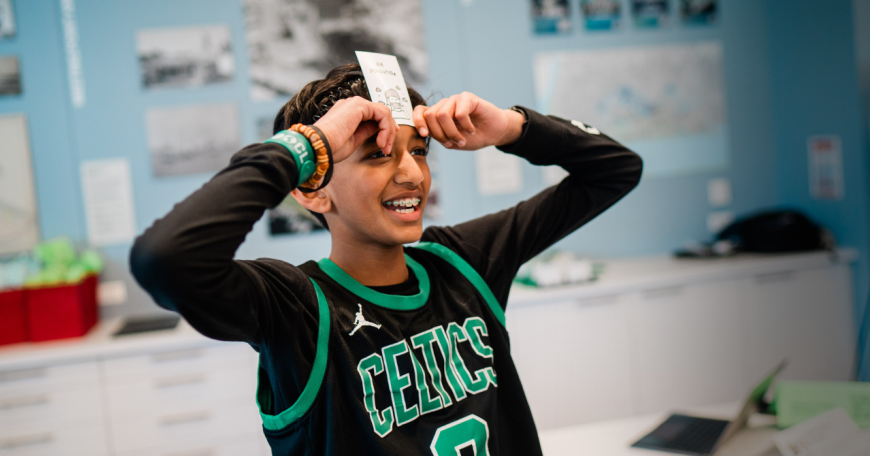 A boy wearing a Celtics jersey holds a card to his forehead