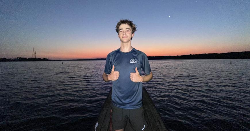 Photo of a teenager posing in front of a body of water with two thumbs up. 