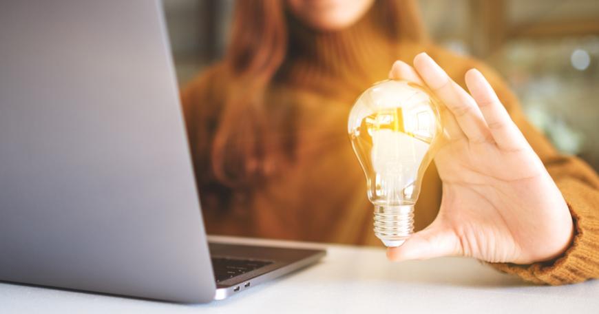 Woman holding a shining lightbulb next to a laptop