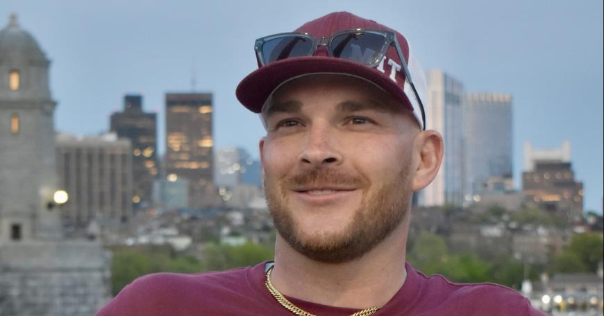 Joshua Gayman smiling wearing a maroon MIT baseball hat