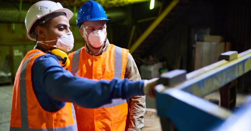 technician wearing reflective vest pointing at something while discussing results of joint work with his colleague