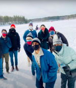 Multiethnic group of men and women dressed in winter wear and face masks, standing on a frozen lake.