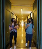 Two students in face masks stand at a distance from each other while exiting the Infinite Corridor.