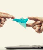 Photo of hand sticking out of a laptop to pass origami rocket to someone else.