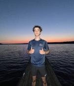 Photo of a teenager posing in front of a body of water with two thumbs up. 