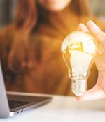 Woman holding a shining lightbulb next to a laptop