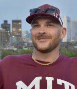 Joshua Gayman smiling wearing a maroon MIT baseball hat
