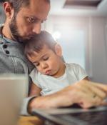 Father kisses the head of sleeping child while working on a laptop