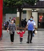 A couple hold the hands of their young child as the three, all masked, walk through an outdoor shopping center.